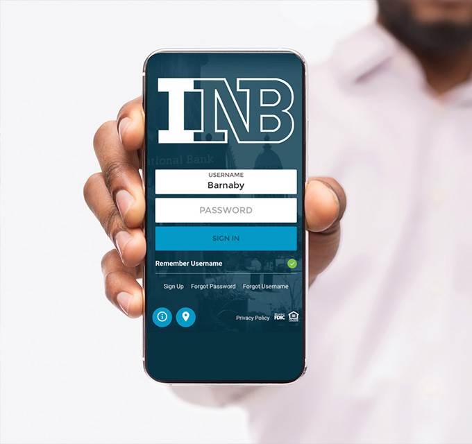 A man holding a smartphone that shows the login screen for the INB app